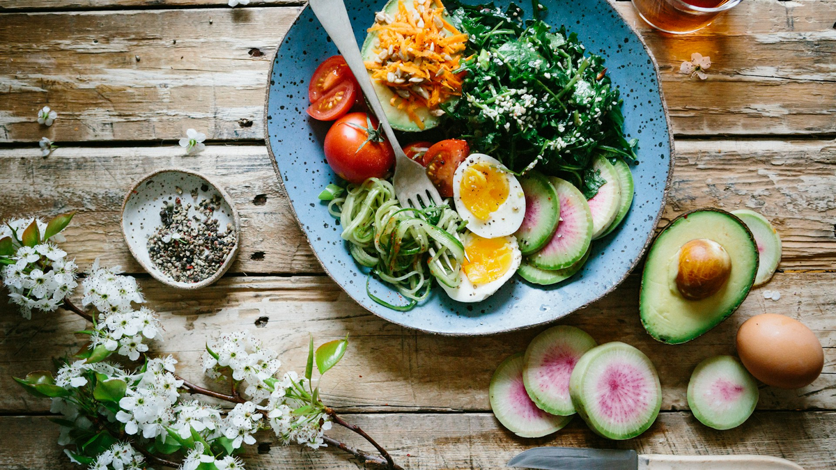 Bowl of salad with boiled eggs, avocado, greens and radish on a rustic wooden table
