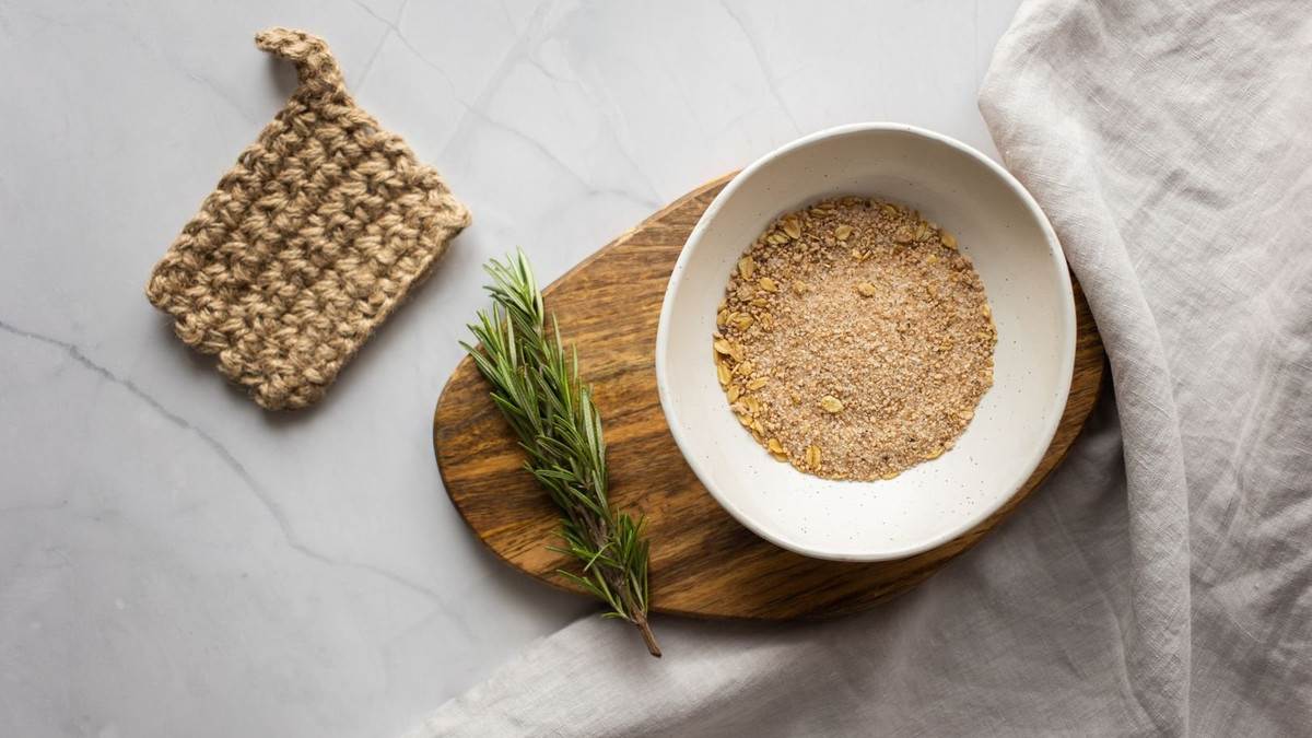 Natural loofah, a bowl of oats and a sprig of rosemary on a wooden board, simple low-chemical bathroom essentials