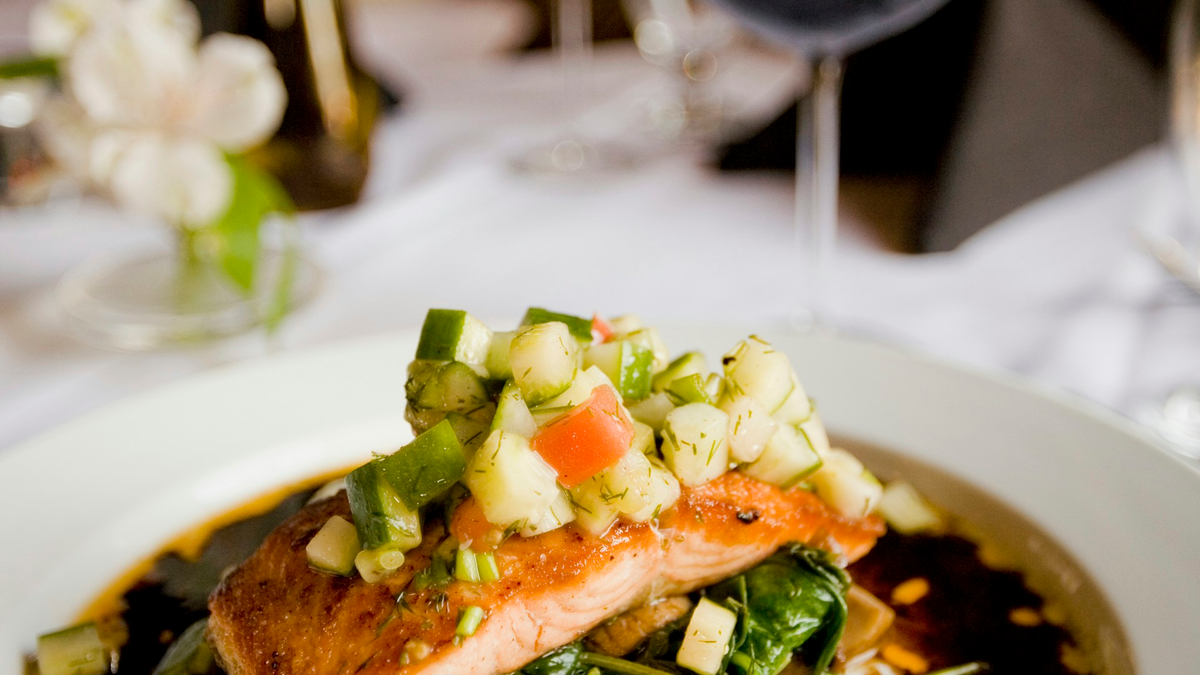 Salmon fillet topped with diced vegetables, served on a white plate