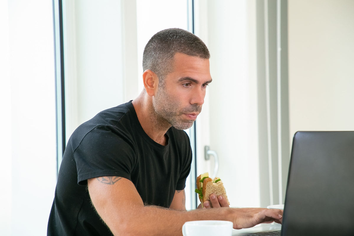Man eating a sandwich at his desk while working, the lunch that often comes before the afternoon slump
