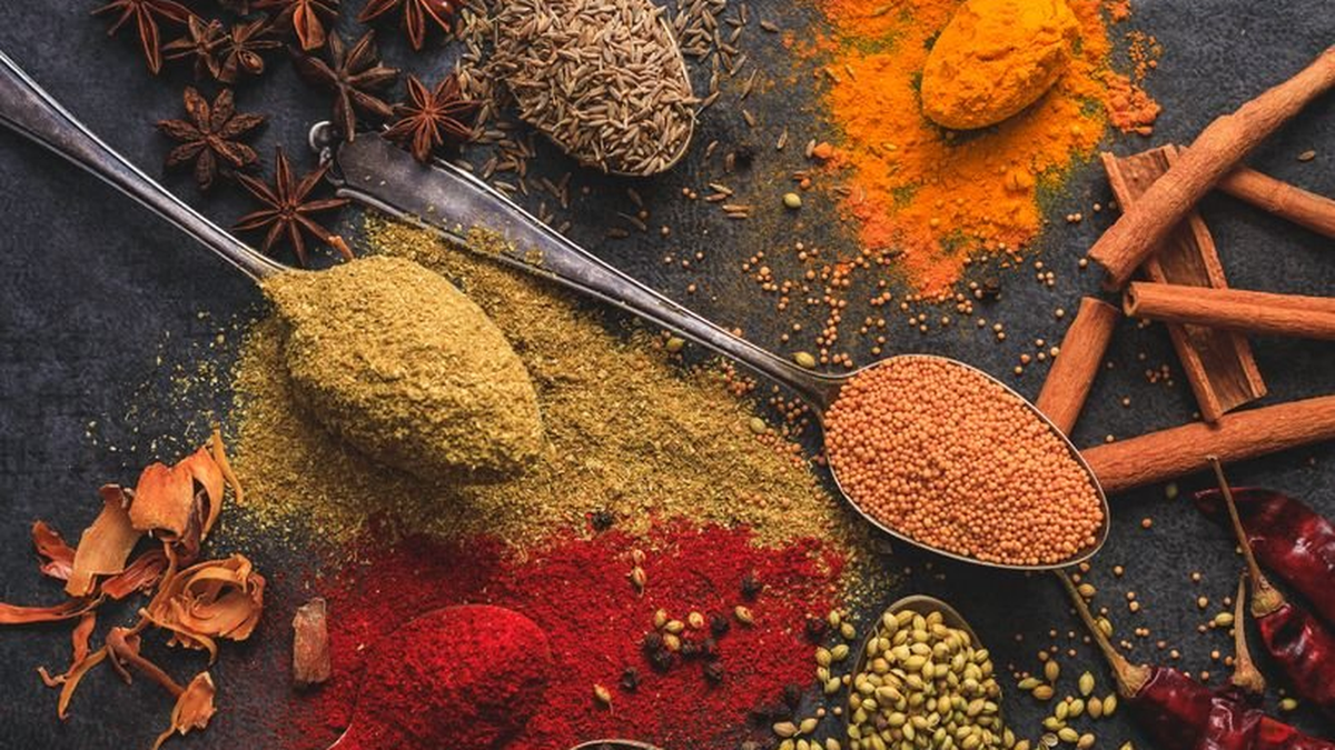 Spoons of colourful ground spices, turmeric and cinnamon sticks on a dark surface