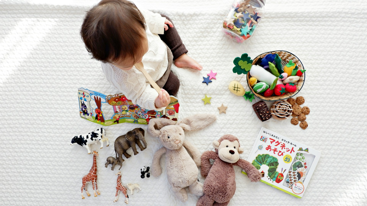 Toddler playing with soft toys and picture books on a white rug, seen from above