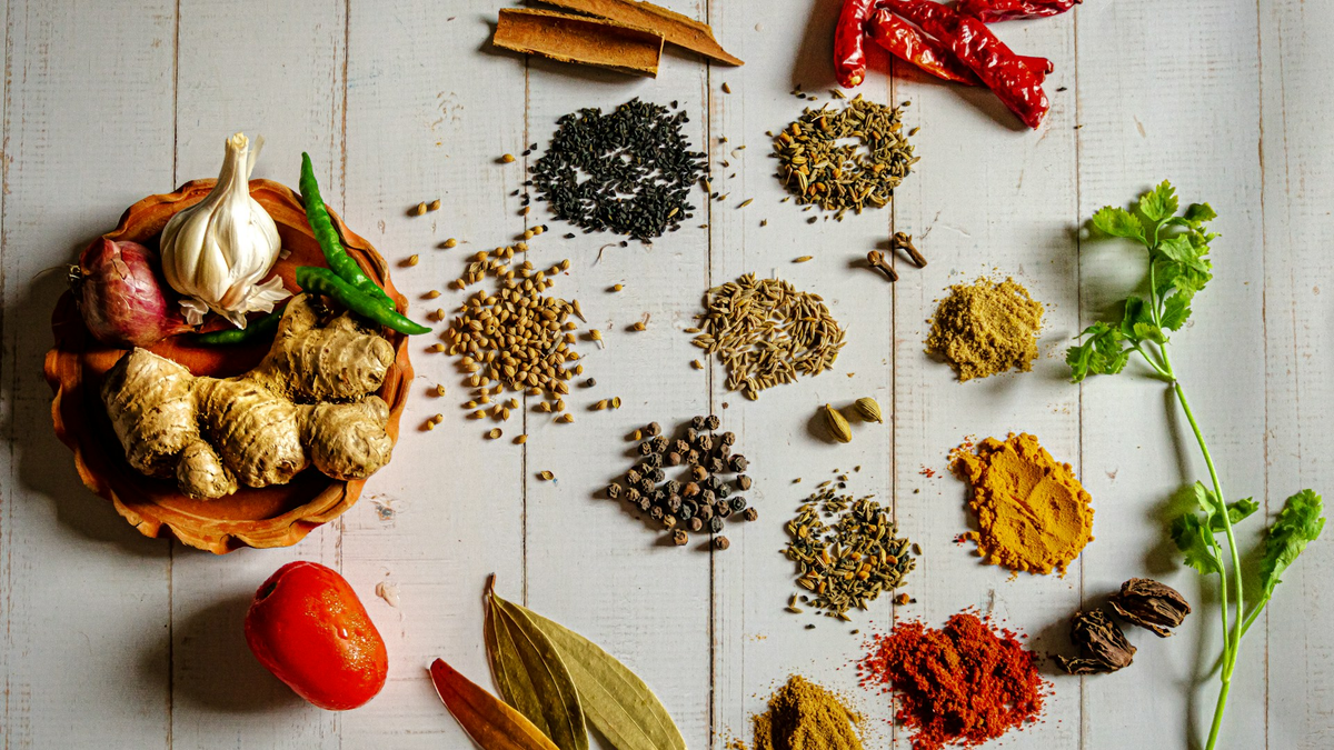 Flat lay of whole spices, seeds, ginger, garlic and fresh herbs on white wood