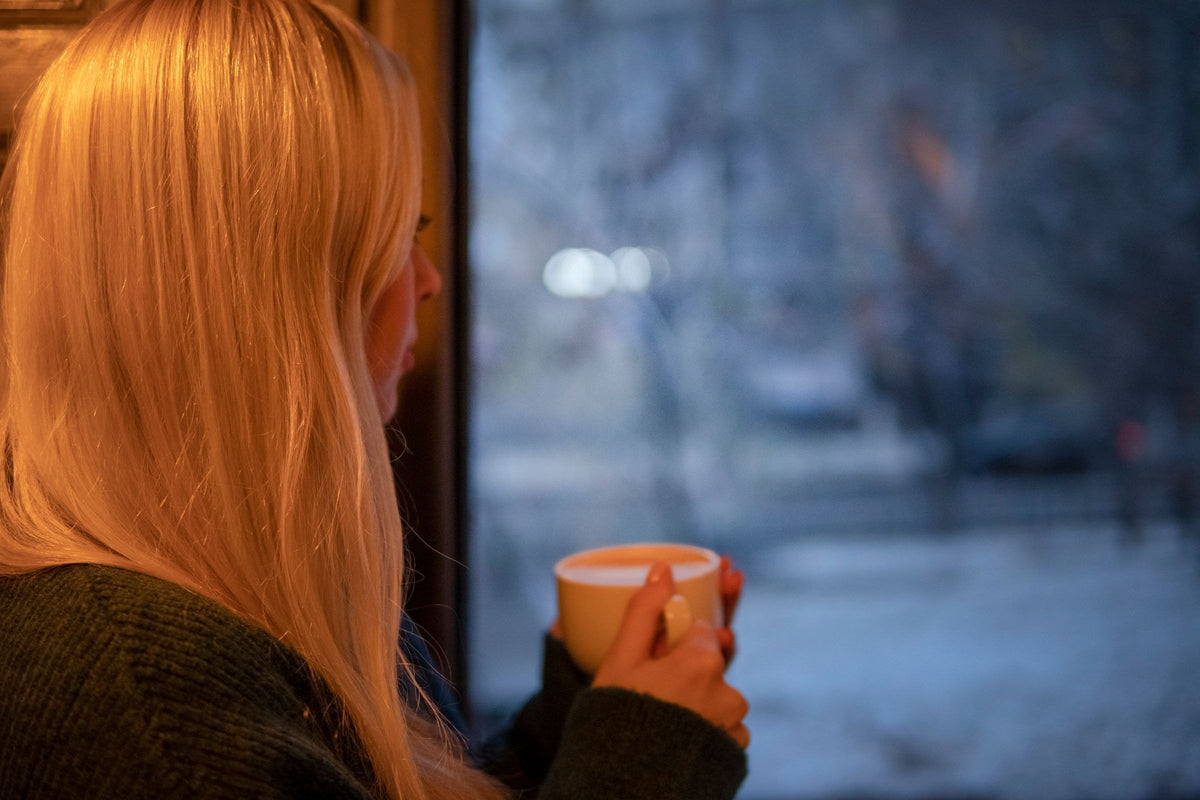 Woman holding a warm mug by the window on a grey winter day