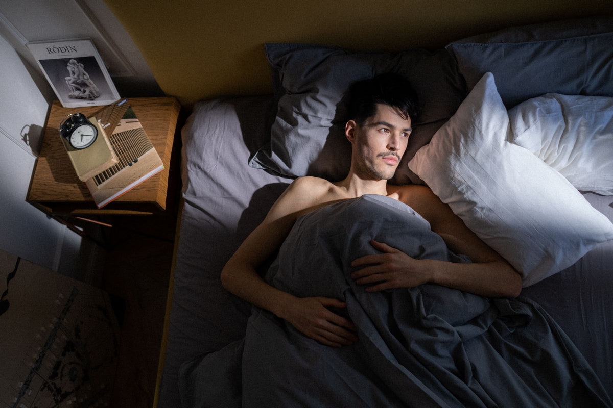 Man lying in bed in early morning light, waking up still feeling tired