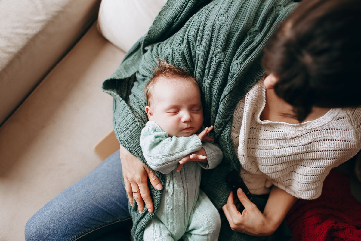 Mother resting on the sofa with her sleeping newborn, the tiring early weeks after having a baby